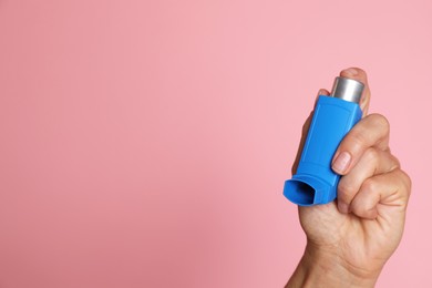 Woman holding asthma inhaler on pink background, closeup. Space for text