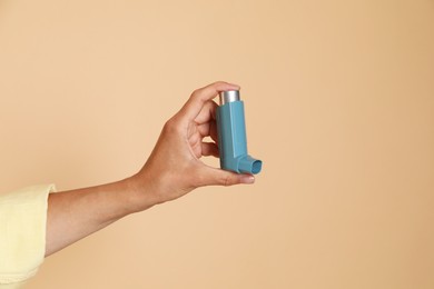 Photo of Woman holding asthma inhaler on beige background, closeup