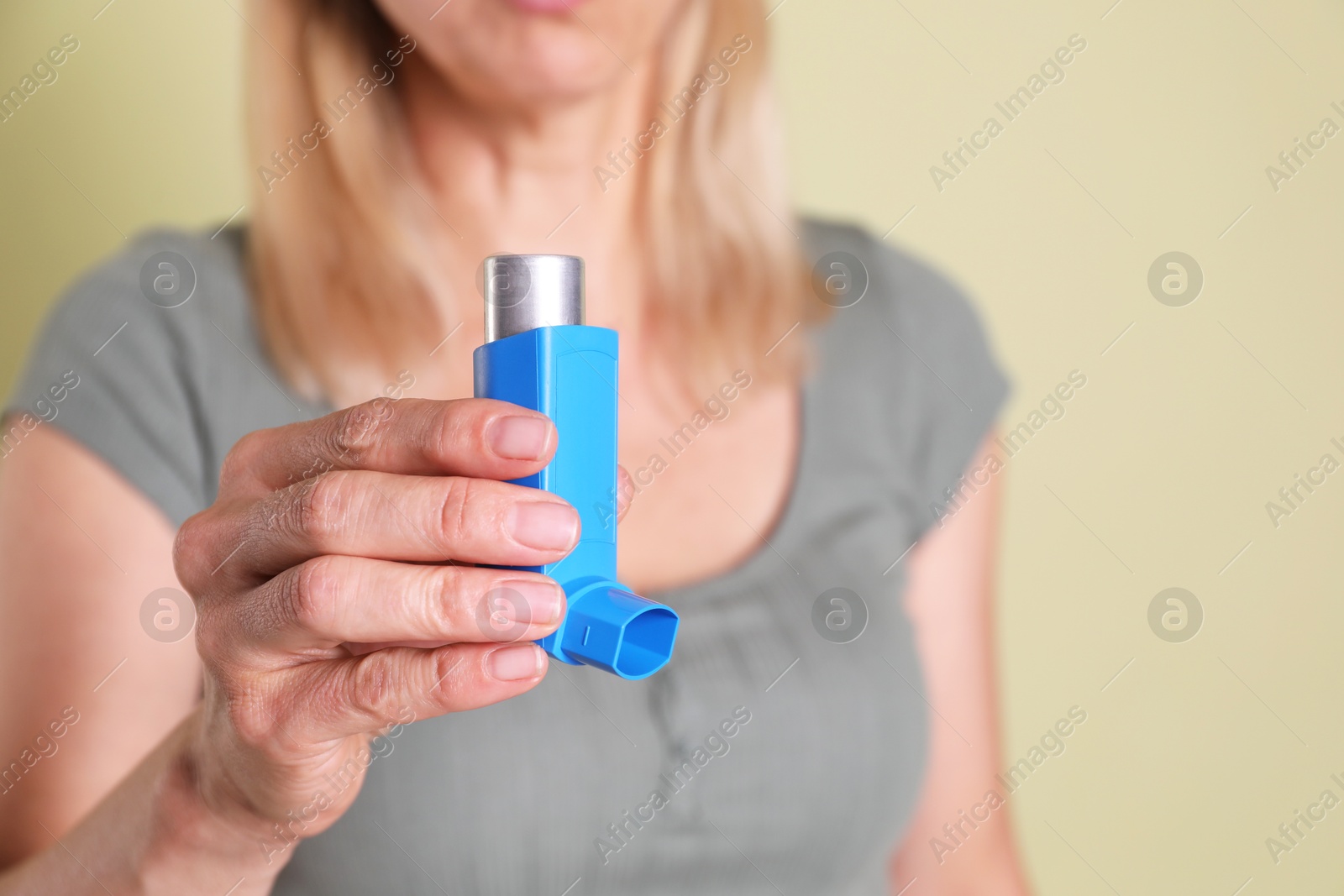 Photo of Woman holding asthma inhaler on olive background, closeup