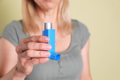 Photo of Woman holding asthma inhaler on olive background, closeup