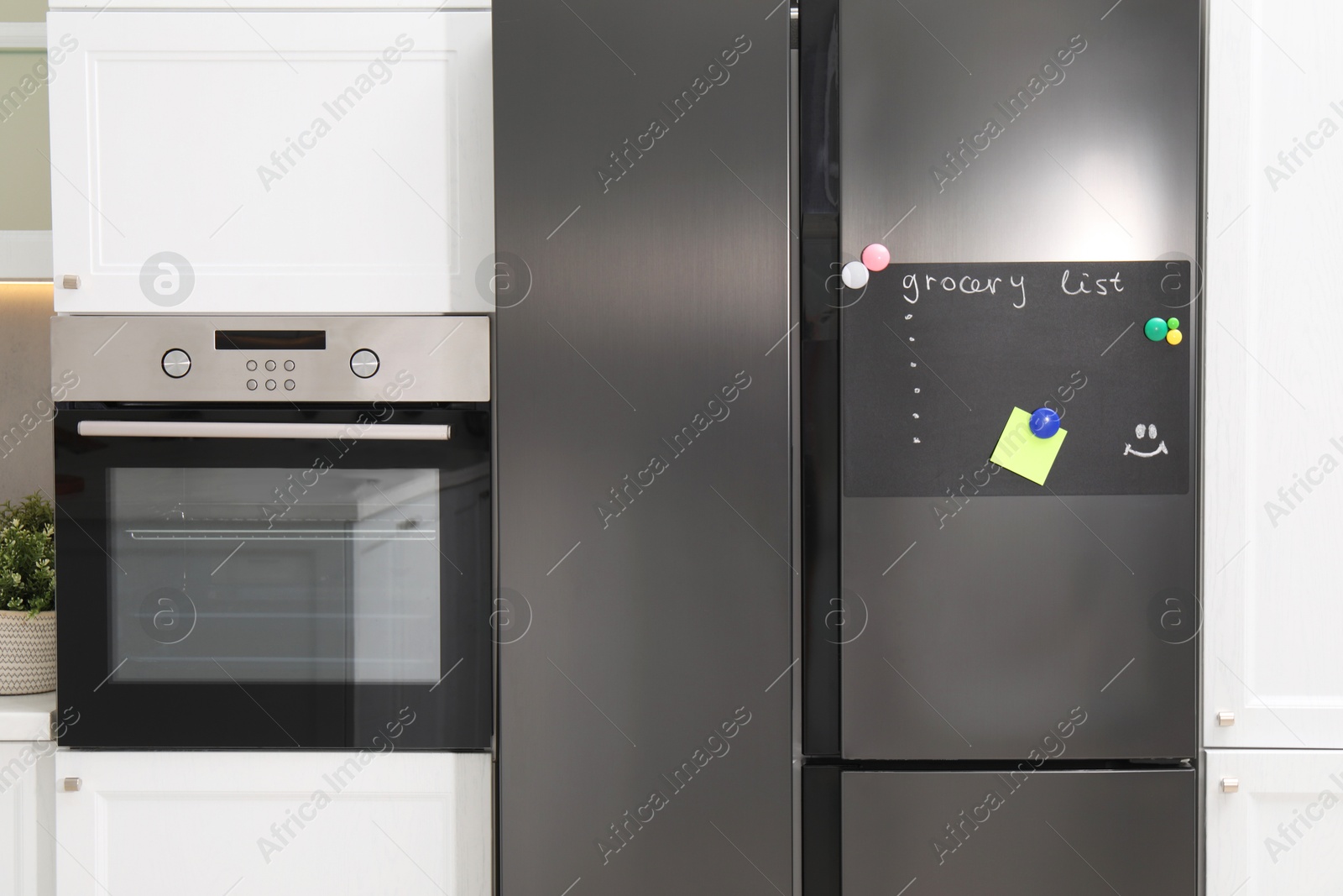 Photo of Magnetic board with grocery list and note on refrigerator in kitchen