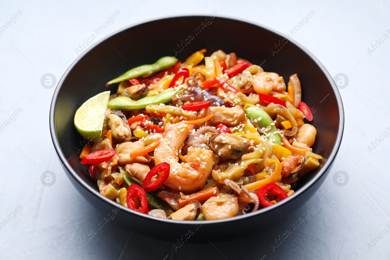 Photo of Stir-fry sea food in bowl on light grey table, closeup