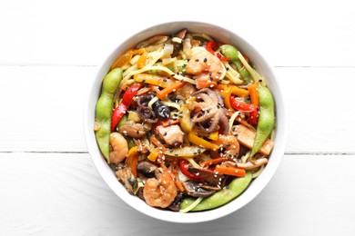 Stir-fry noodles with sea food in bowl on white wooden table, top view