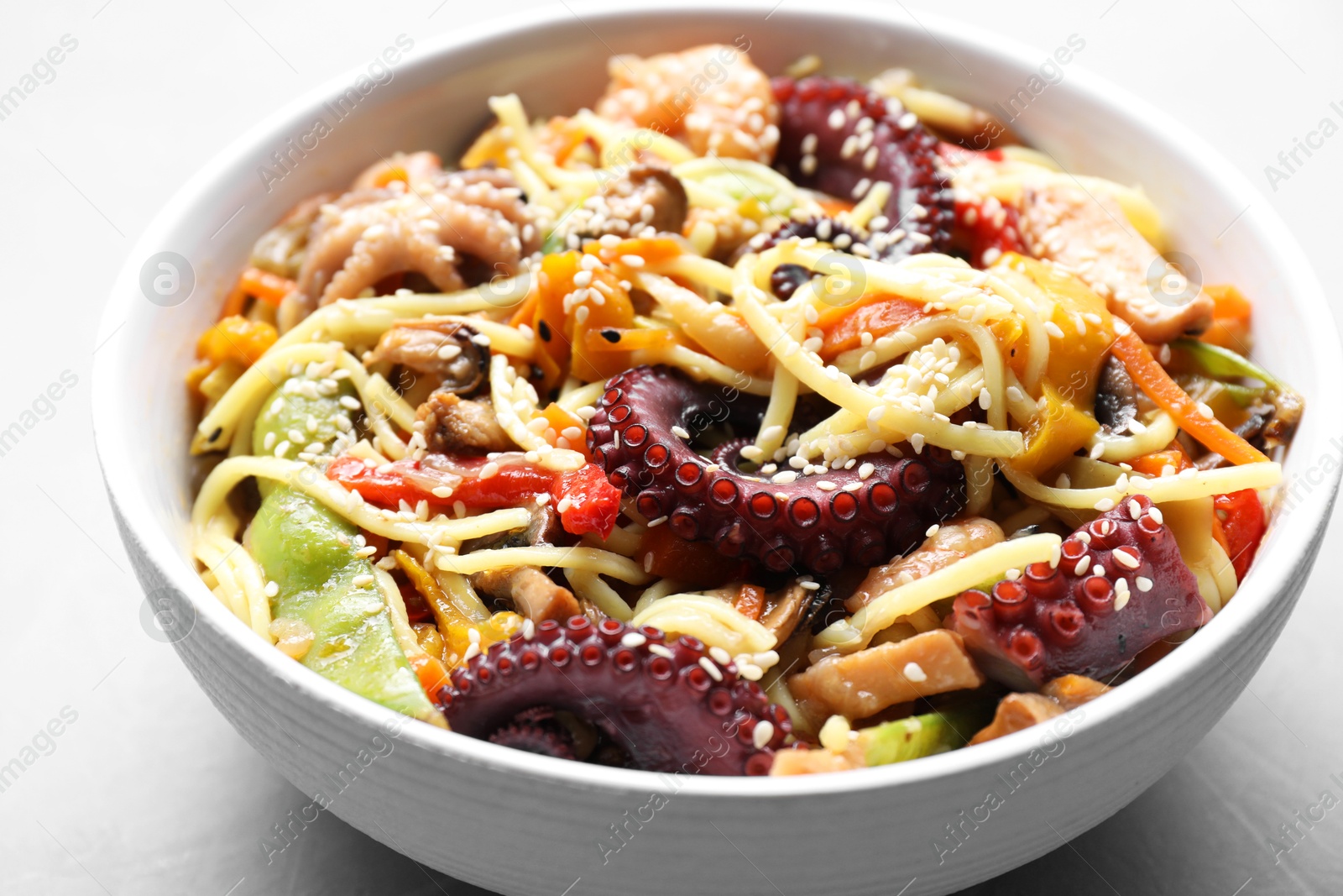 Photo of Stir-fry noodles with sea food in bowl on light grey table, closeup