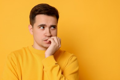 Portrait of scared young man on orange background, space for text