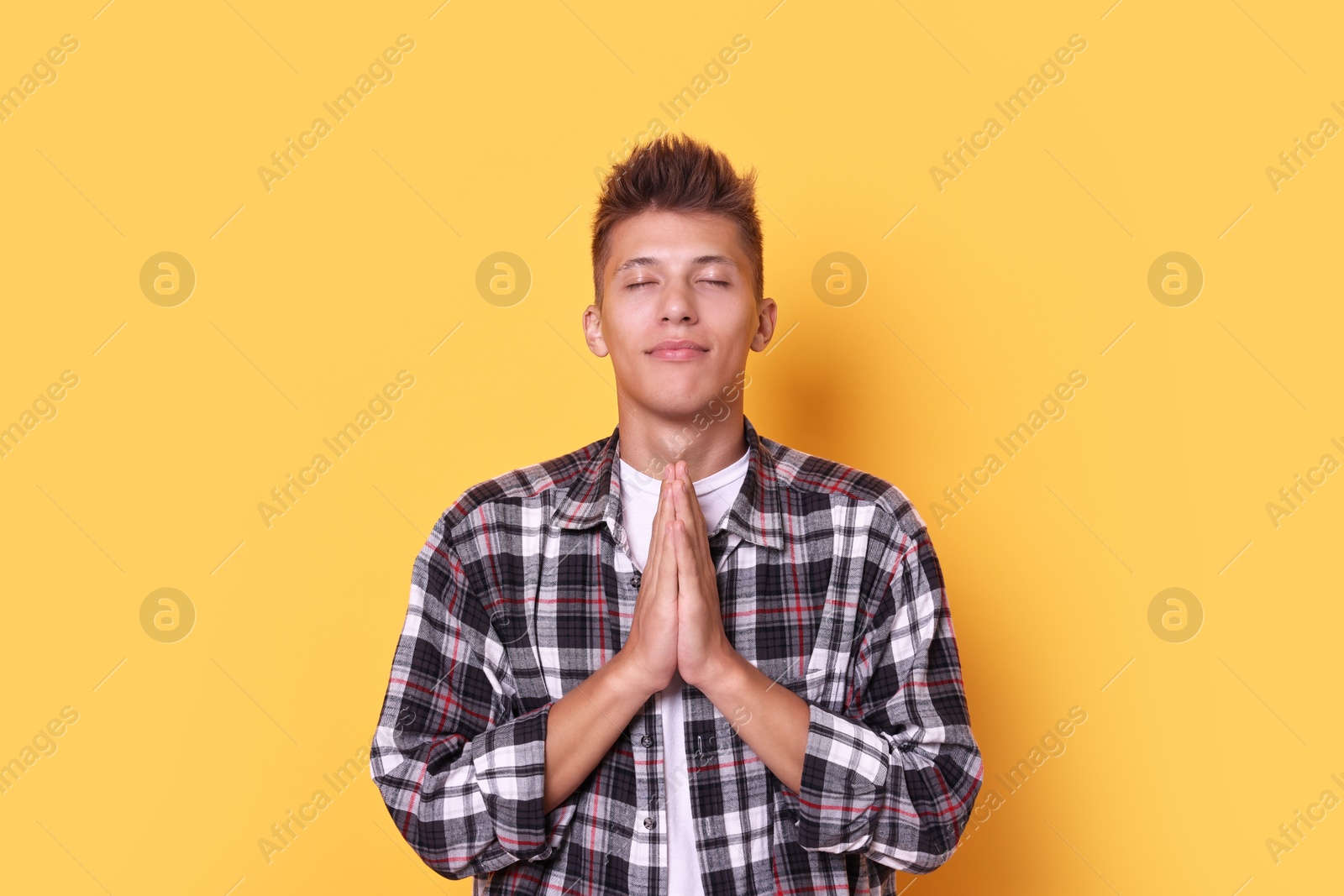 Photo of Young student praying for good exam result on yellow background