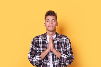 Young student praying for good exam result on yellow background