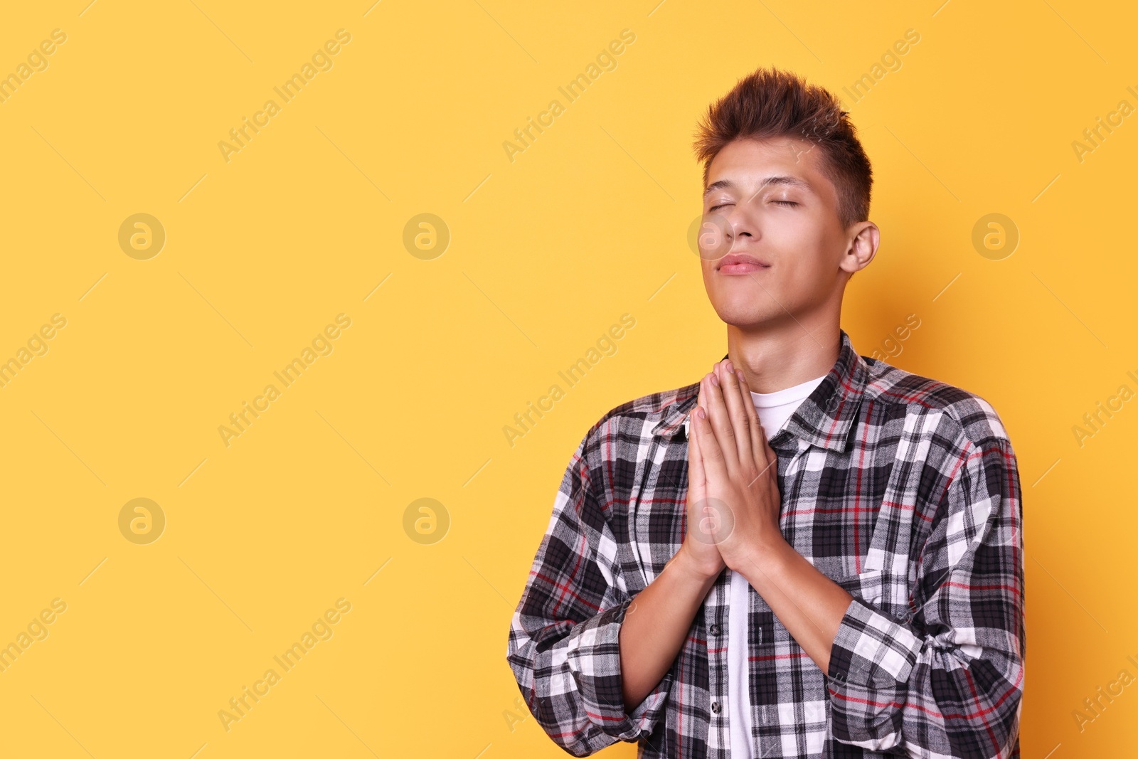 Photo of Young student praying for good exam result on yellow background, space for text