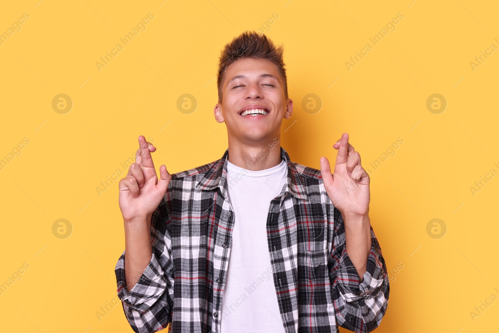 Photo of Excited young student crossing fingers on yellow background. Hope for good exam result