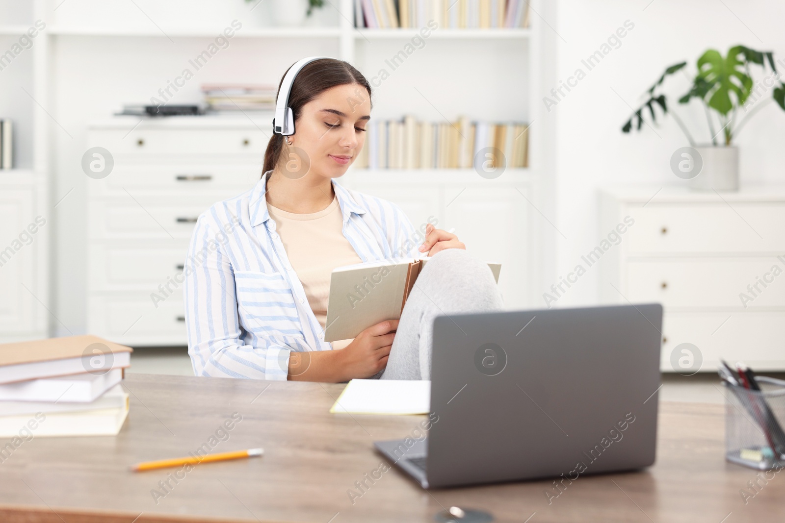 Photo of Student in headphones studying at wooden table indoors