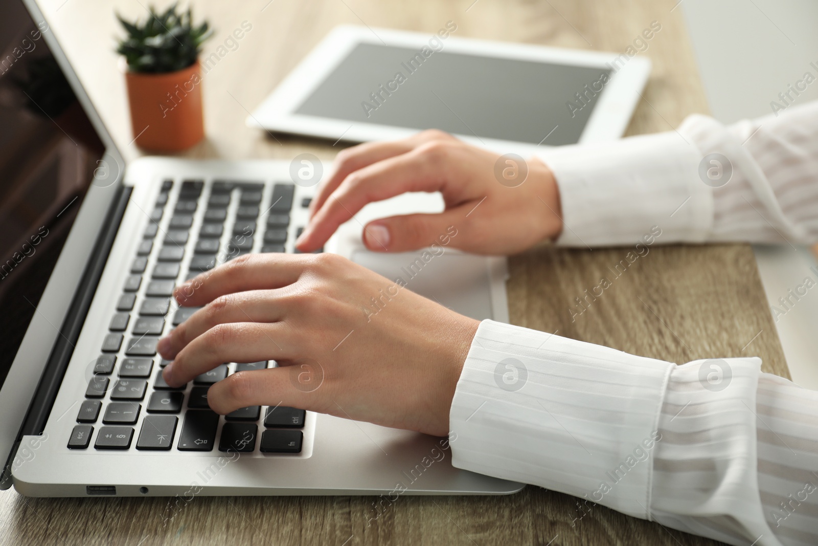 Photo of Businesswoman using laptop at wooden table indoors, closeup. Modern technology