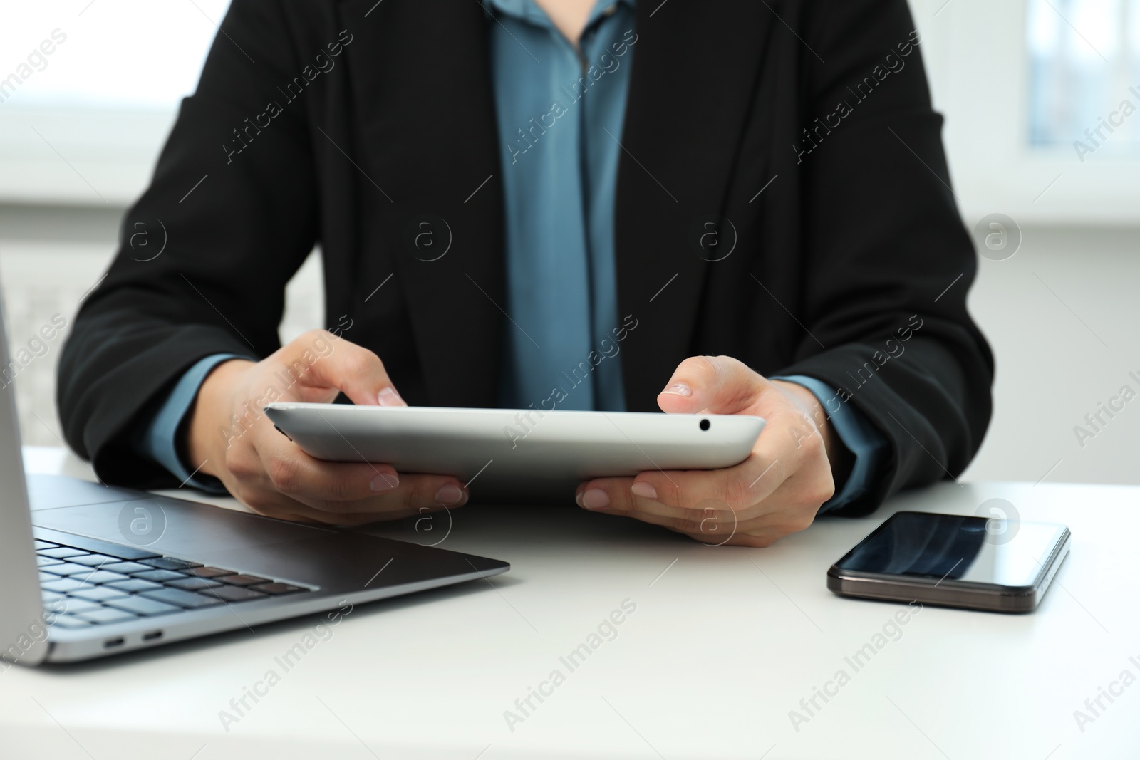 Photo of Businesswoman using tablet at white table indoors, closeup. Modern technology