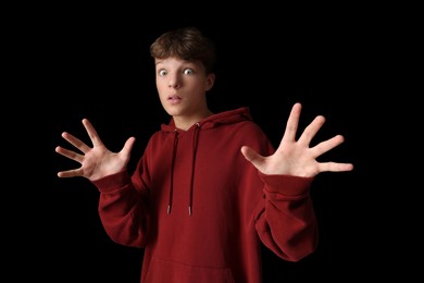 Portrait of scared teenage boy on black background