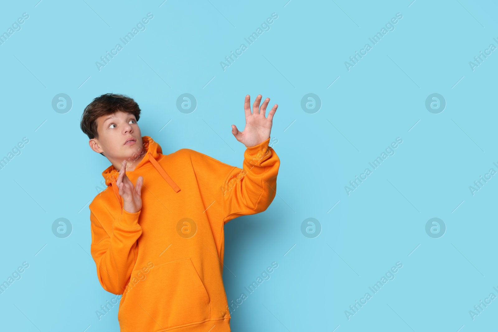 Photo of Scared teenage boy on light blue background. Space for text