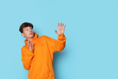 Photo of Scared teenage boy on light blue background. Space for text