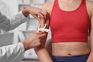 Photo of Doctor measuring woman's body fat with caliper in clinic, closeup