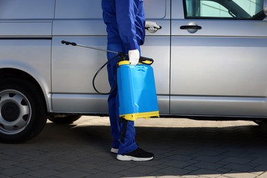 Photo of Pest control worker with spray tank near gray minibus outdoors, closeup