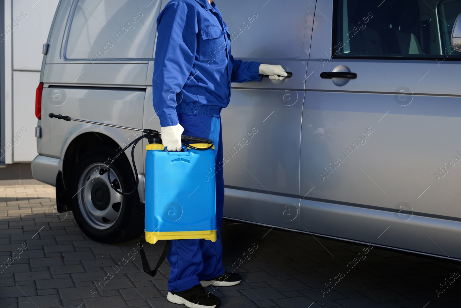 Photo of Pest control worker with spray tank near gray minibus outdoors, closeup