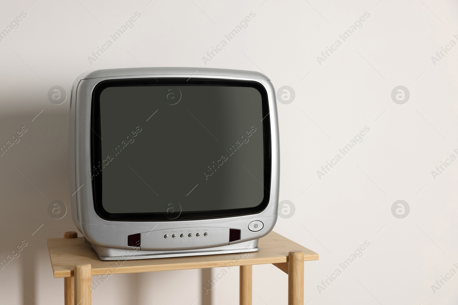 Photo of Retro tv set on wooden shelf against white wall. Space for text