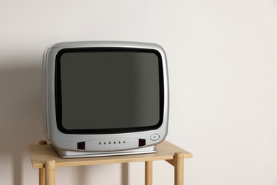 Photo of Retro tv set on wooden shelf against white wall. Space for text