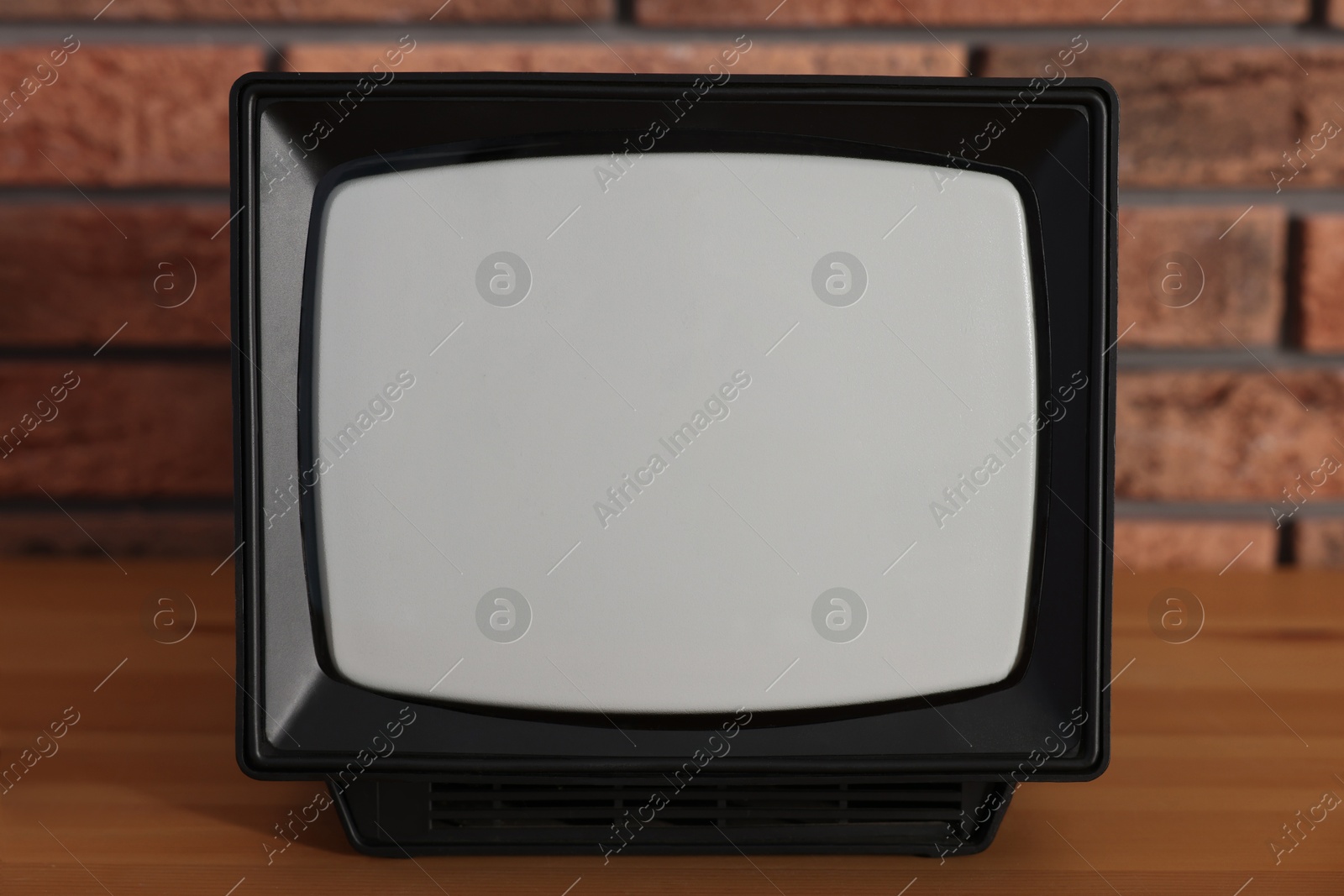 Photo of Retro tv set on wooden shelf against red brick wall