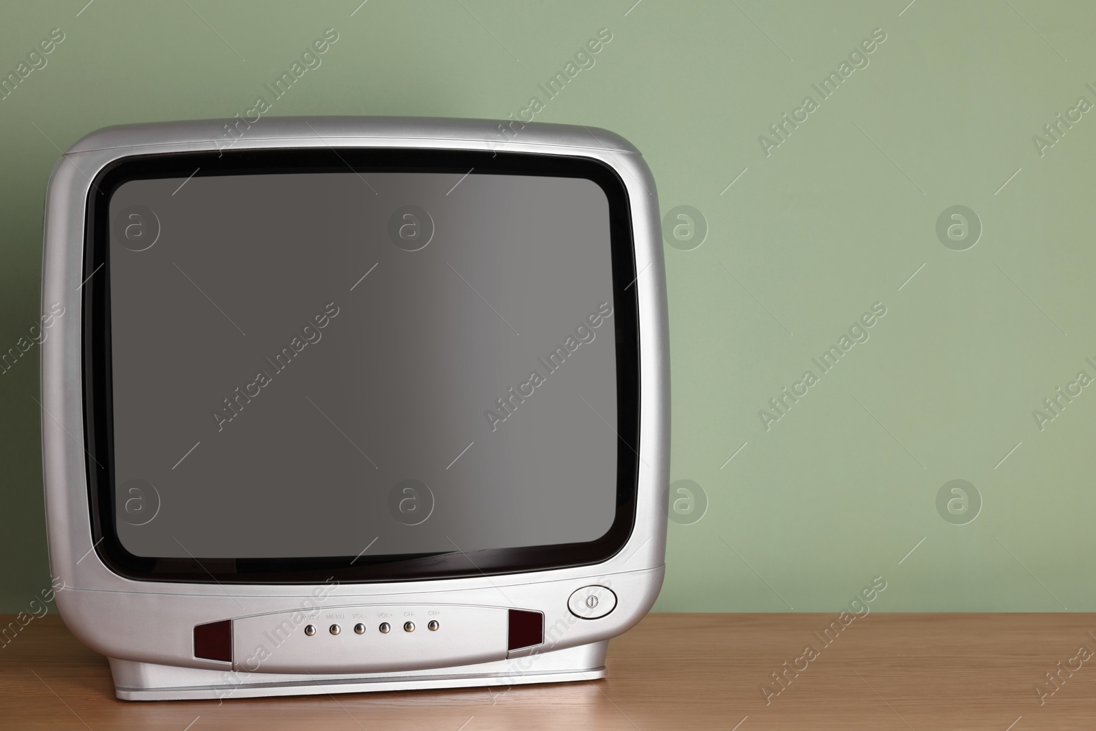 Photo of Retro tv set on wooden shelf against green wall. Space for text