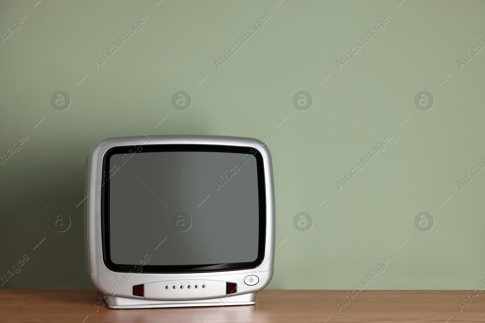 Photo of Retro tv set on wooden shelf against green wall. Space for text