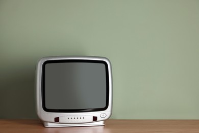 Photo of Retro tv set on wooden shelf against green wall. Space for text