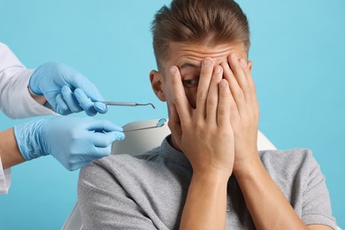 Dental phobia. Dentist working with scared man on light blue background, closeup