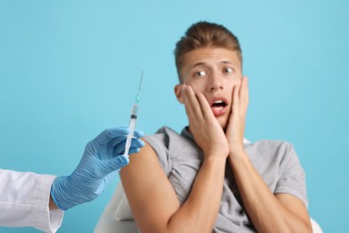 Needle phobia. Doctor with syringe near scared man on light blue background, closeup