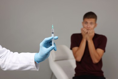 Photo of Needle phobia. Doctor with syringe near scared man on grey background, selective focus