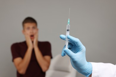 Photo of Needle phobia. Doctor with syringe near scared man on grey background, selective focus