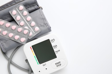 Photo of Blood pressure measuring device and pills on white background, top view. Space for text