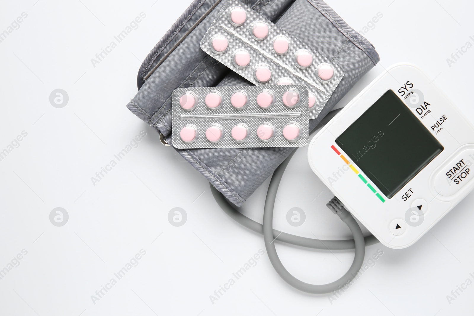 Photo of Blood pressure measuring device and pills on white background, top view. Space for text