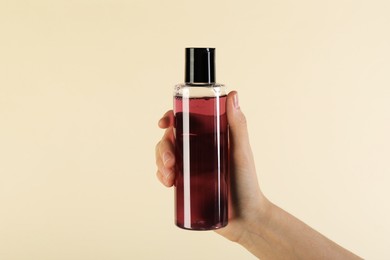 Photo of Woman with shampoo bottle on beige background, closeup