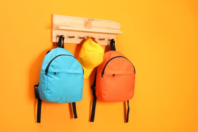 Photo of Bright backpacks and cap hanging on orange wall