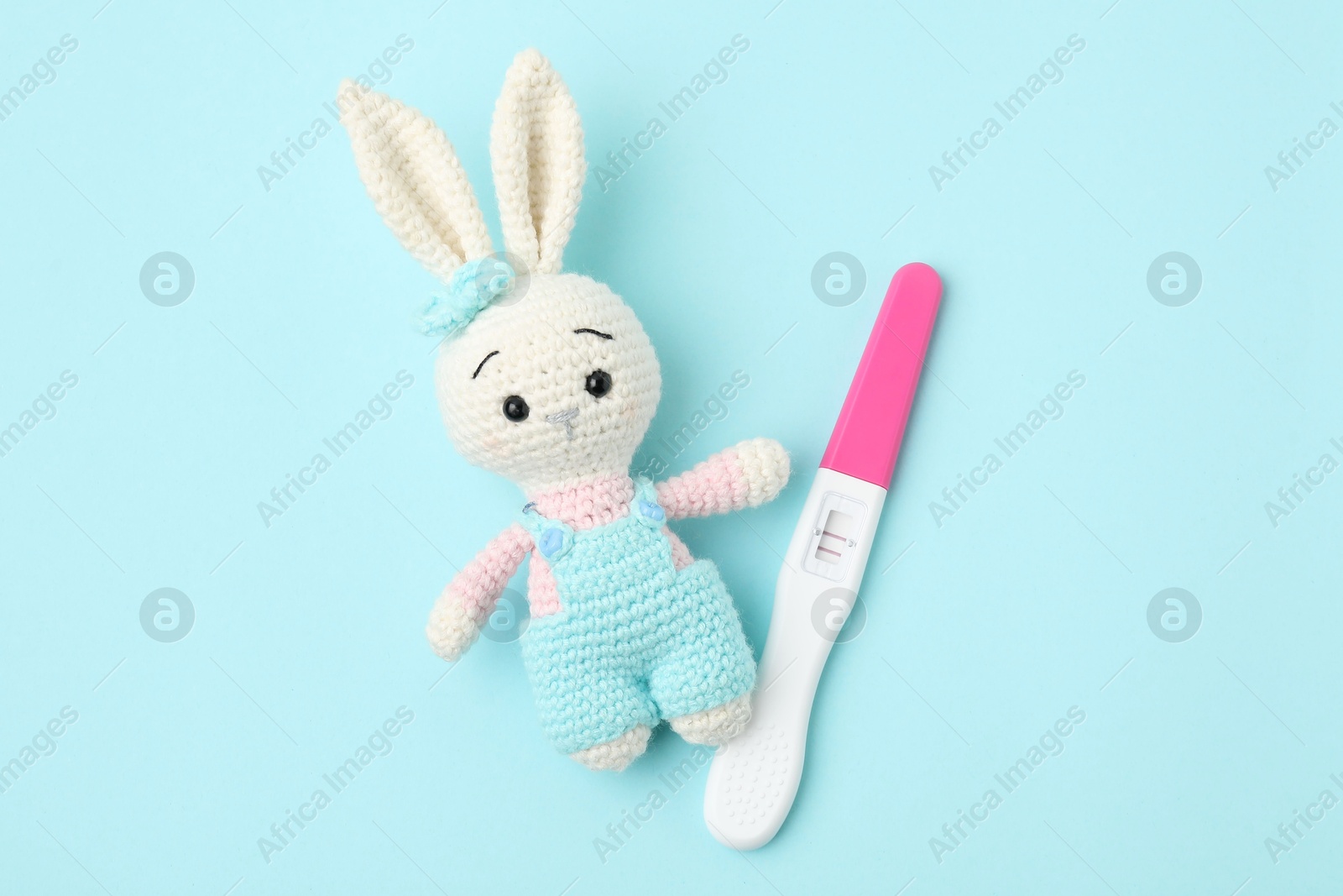 Photo of Pregnancy test and toy bunny on light blue background, top view