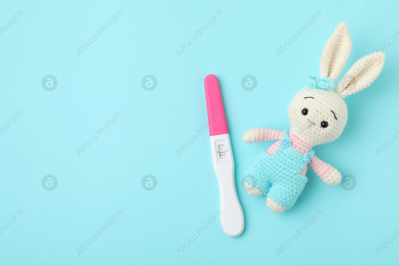 Photo of Pregnancy test and toy bunny on light blue background, top view. Space for text