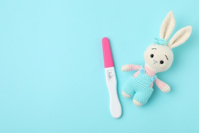 Photo of Pregnancy test and toy bunny on light blue background, top view. Space for text