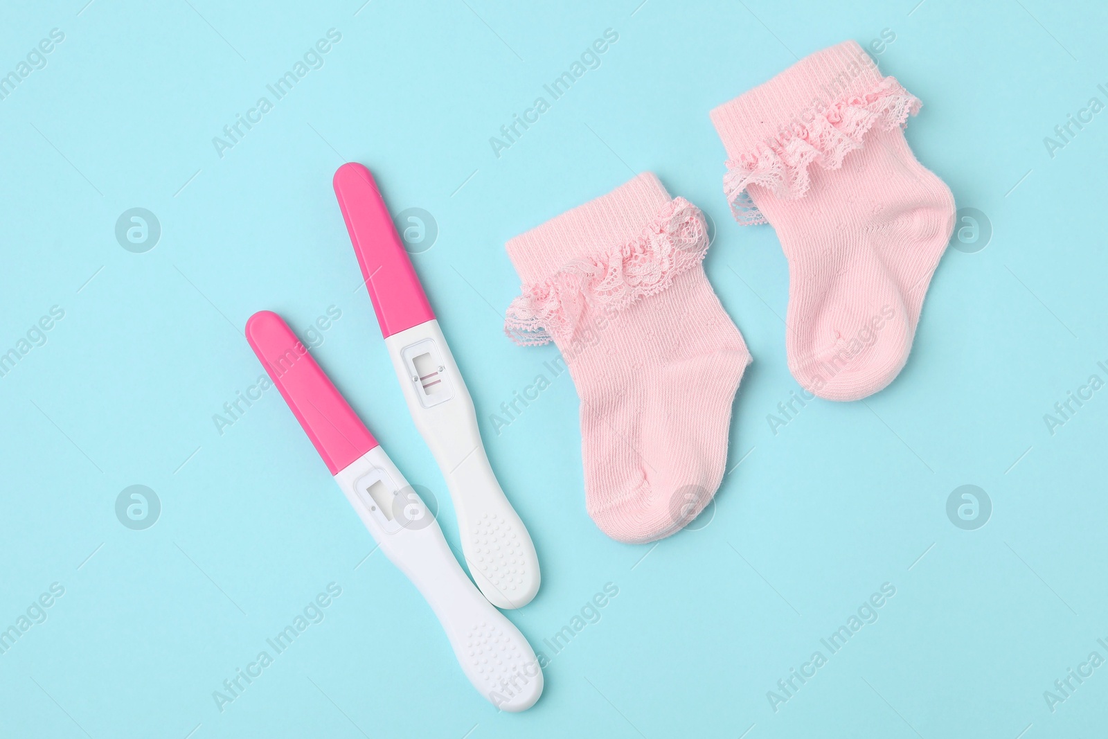 Photo of Pregnancy tests and pink socks on light blue background, top view