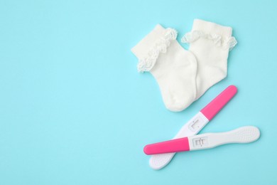 Photo of Pregnancy tests and socks on light blue background, top view. Space for text