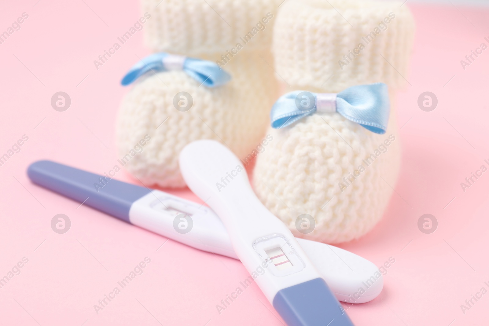 Photo of Pregnancy tests and knitted booties on pink background, closeup