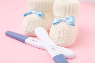 Photo of Pregnancy tests and knitted booties on pink background, closeup