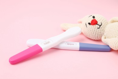 Photo of Pregnancy tests and toy bunny on pink background, closeup