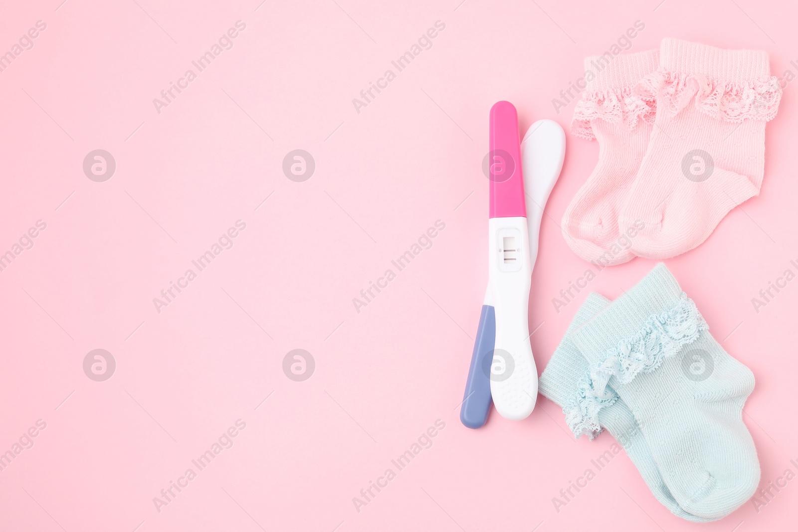 Photo of Pregnancy tests and socks on pink background, top view. Space for text