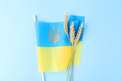 Photo of Ears of wheat and Ukrainian flag on light blue background, top view