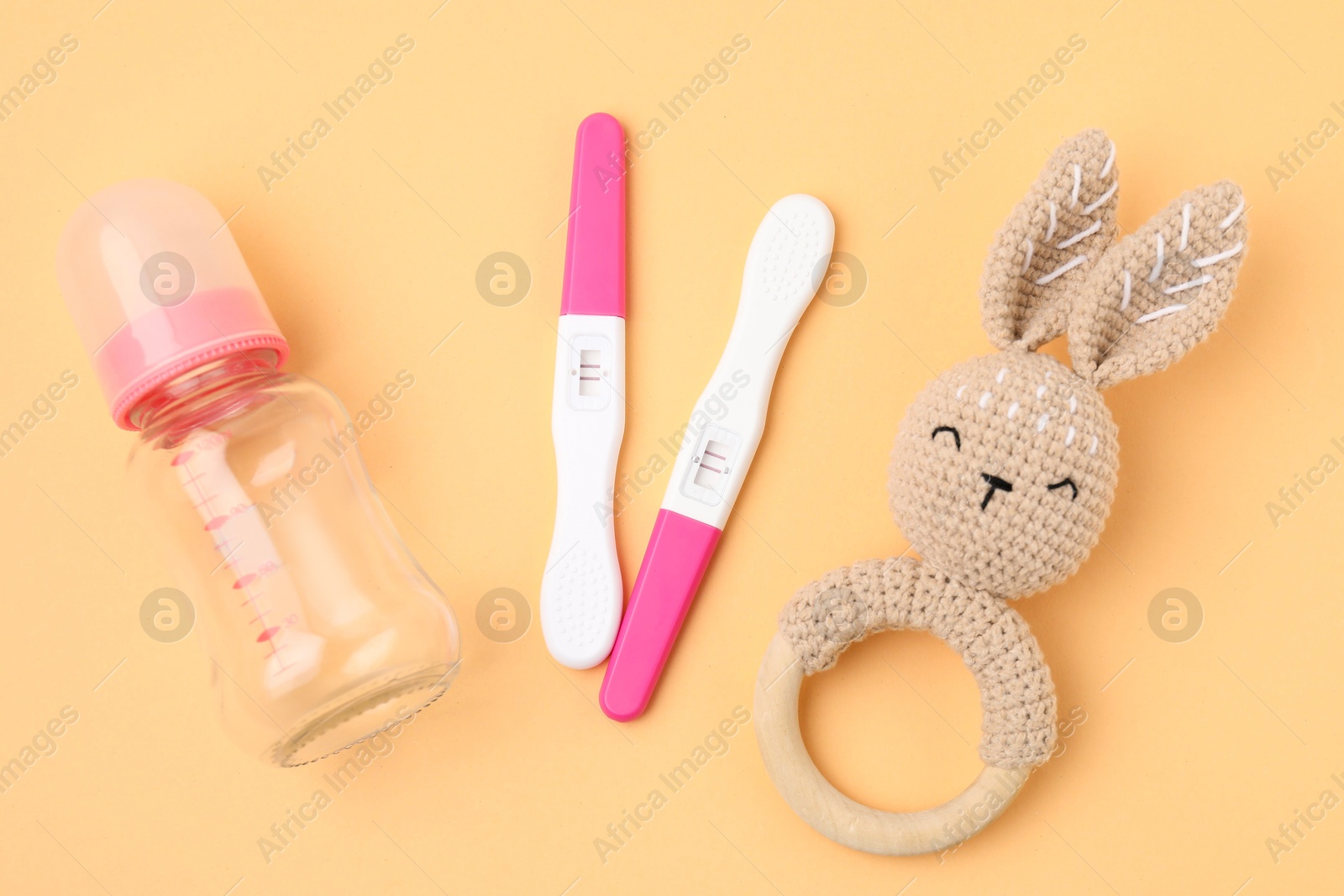 Photo of Pregnancy tests, rattle and baby bottle on pale orange background, flat lay