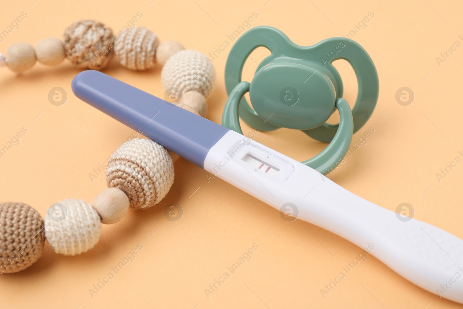 Photo of Pregnancy test, pacifier and teether on pale orange background, closeup