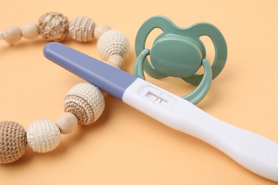 Photo of Pregnancy test, pacifier and teether on pale orange background, closeup