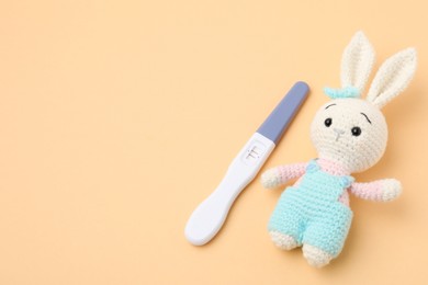 Photo of Pregnancy test and toy bunny on pale orange background, space for text